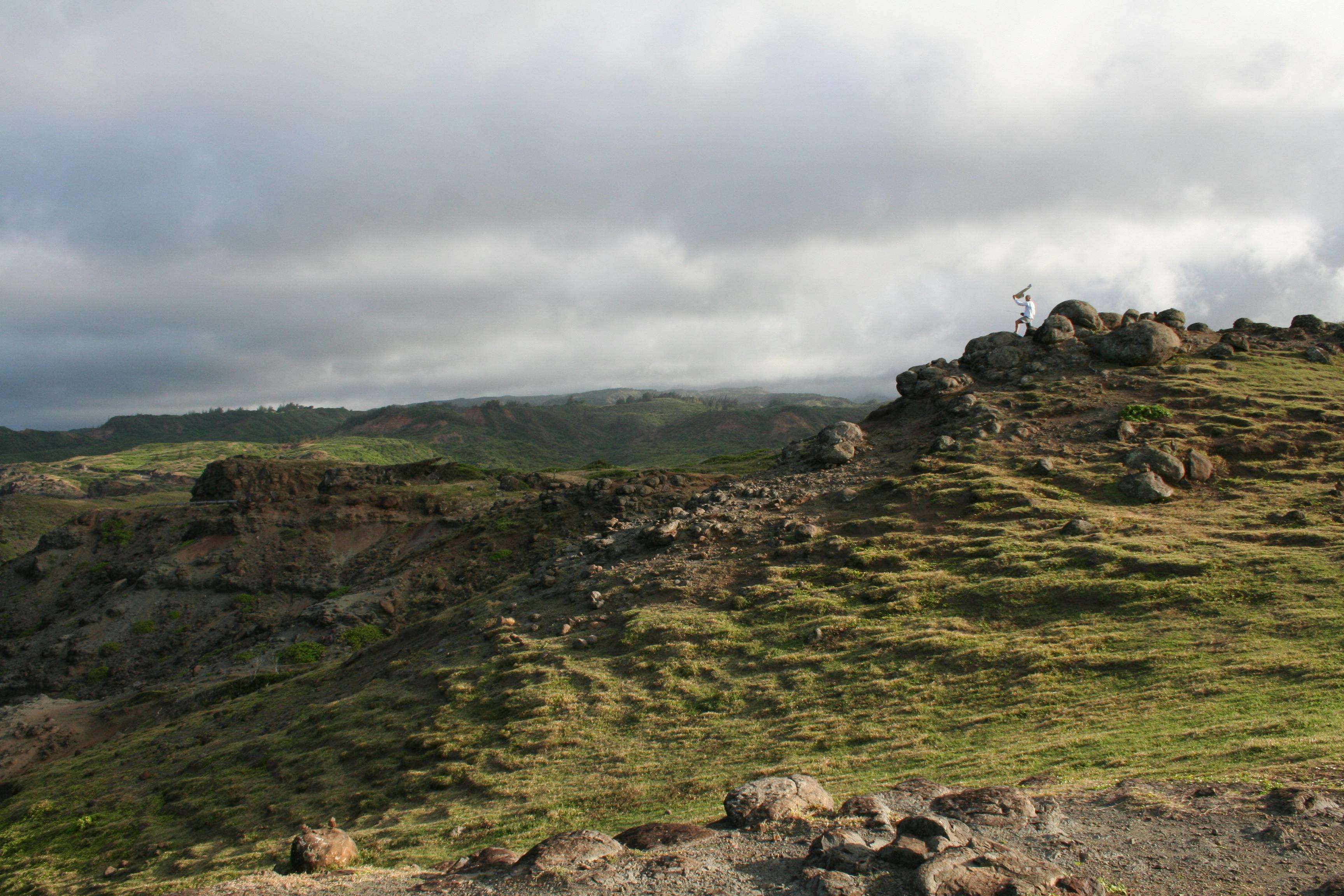 一位孤独的徒步旅行者在云雾弥漫的天空下，探索着岩石与草木交织的景观，捕捉冒险的本质