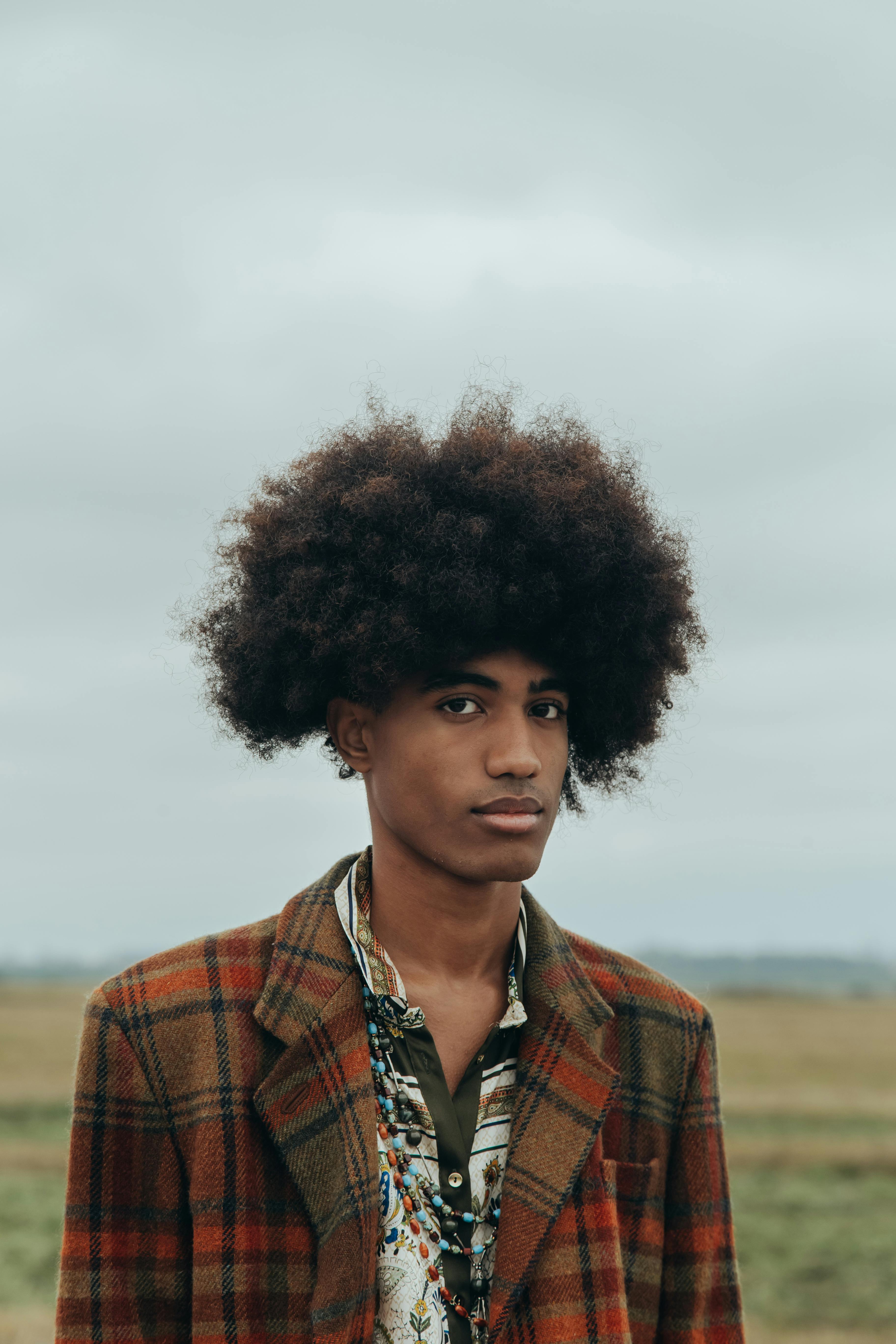 Portrait of a young man with afro hair in a vintage plaid coat posing outdoors.