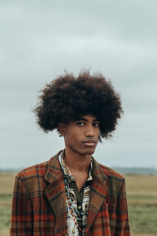A Man with Afro Hair Wearing Plaid Coat while Seriously Looking at the Camera