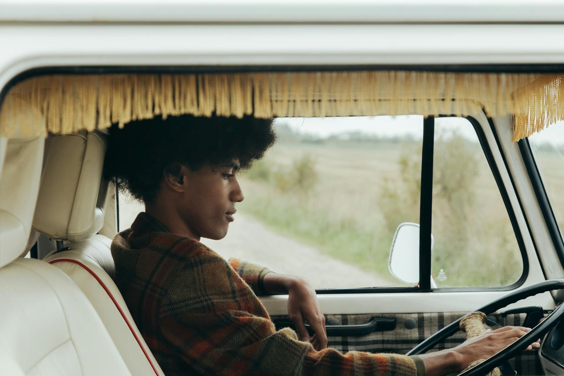 A young man with afro hair sitting in a vintage van, enjoying a road trip in the countryside.