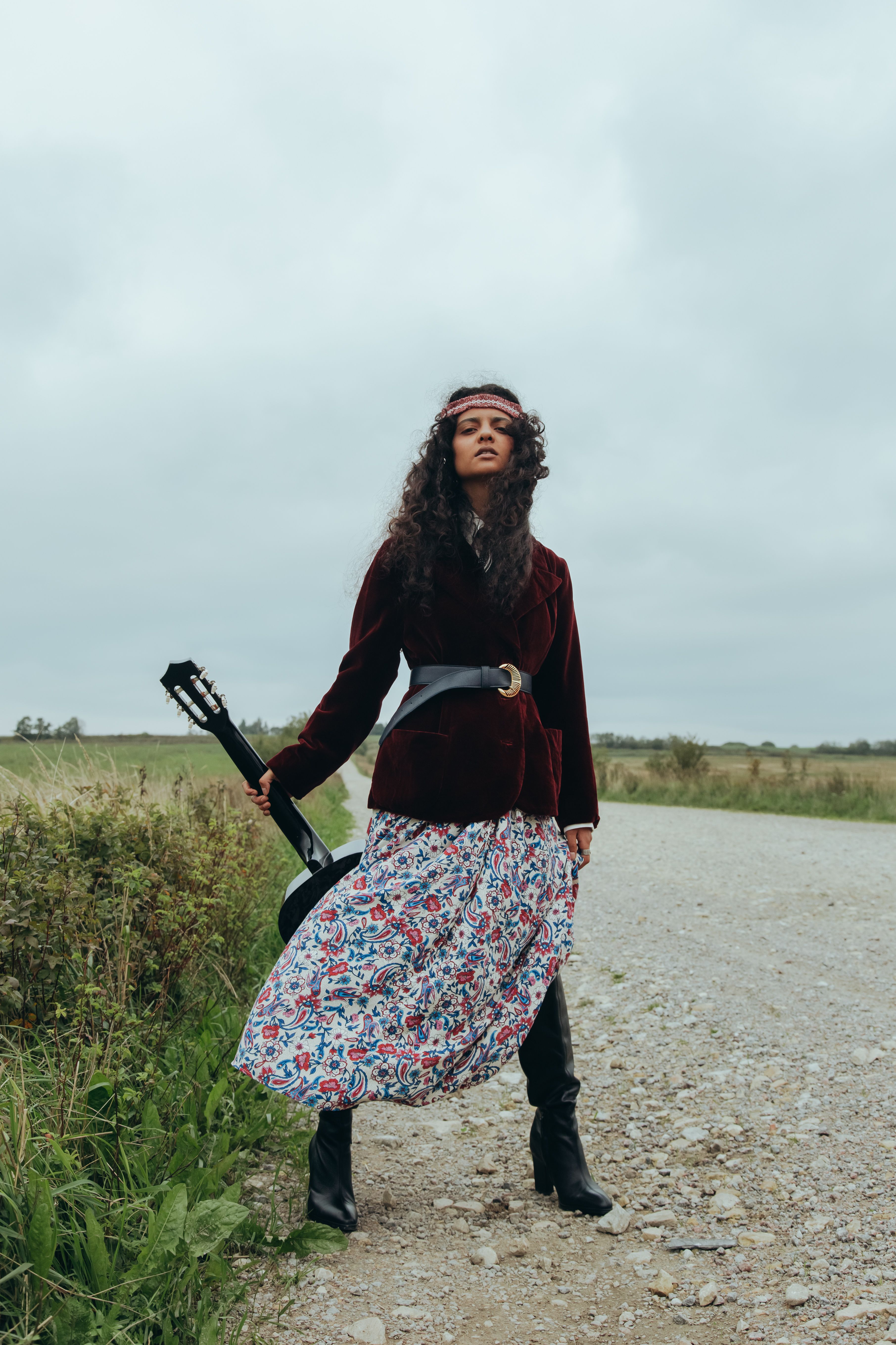 Young woman holding a guitar on a rural path, embracing freedom and style.