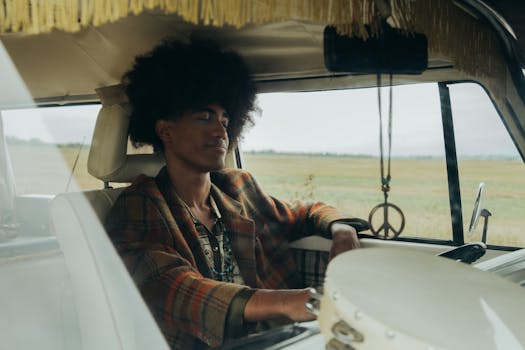 A man with afro hair relaxing in a vintage car with peace symbol decor, embodying a bohemian lifestyle.