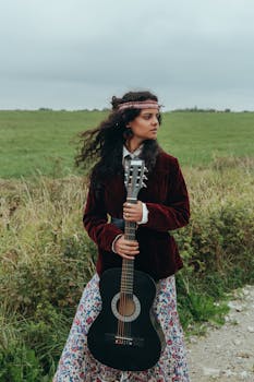 Bohemian woman holding a guitar in an open field, embracing a free-spirited lifestyle.