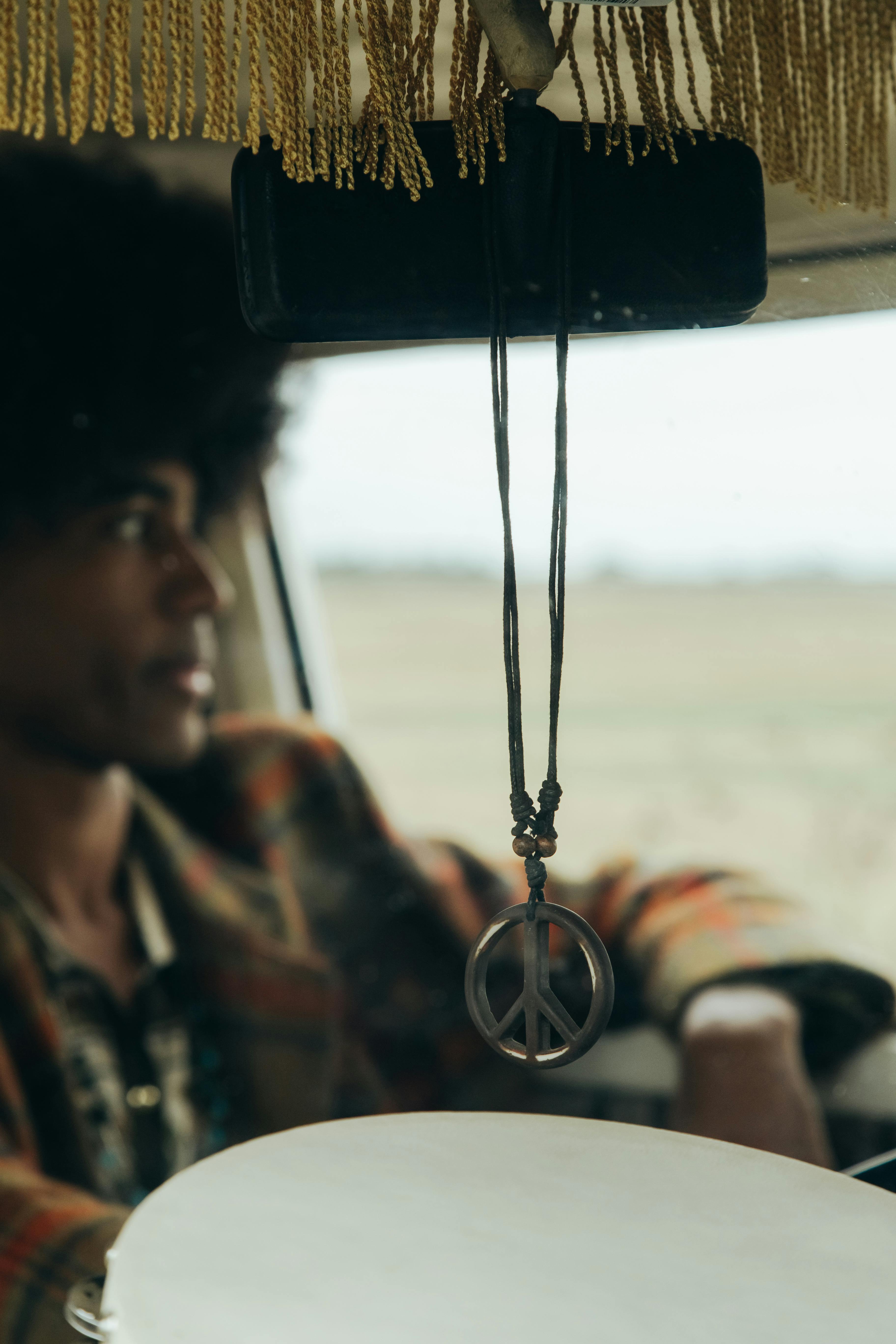 peace sign pendant hanging on a mirror inside a car and man sitting behind the wheel