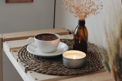 Free Cup of Coffee Lying on Tray with Lit Candle and Glass Vase Stock Photo