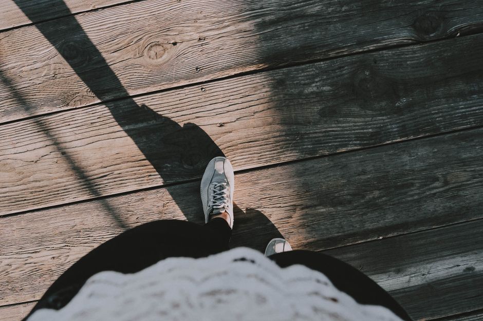 Shadow of a person wearing sneakers walking on rustic wooden planks outdoors with a high angle shot.