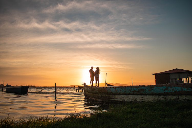 A Couple Standing On Wooden Dock During Sunset