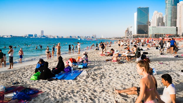 Bustling beach in Dubai with people enjoying the sun and city skyline in the background.