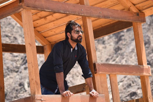 一个男人戴着墨镜，在晴朗的日光下靠在户外的木结构上