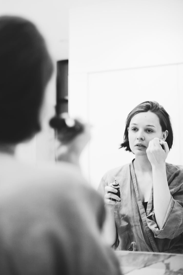 Grayscale Photo Of A Woman Putting Makeup In Front Of A Mirror