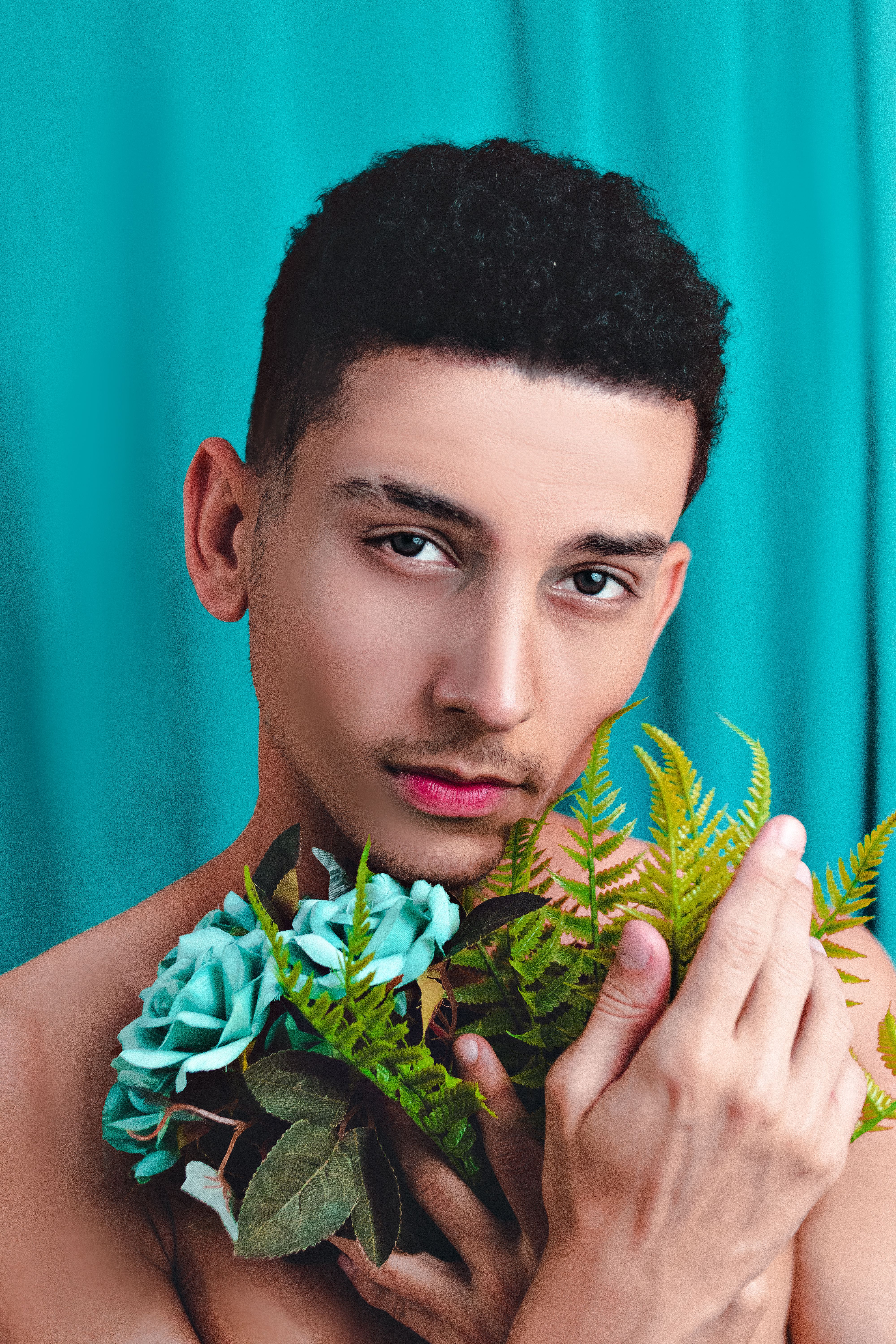 Portrait of a man holding turquoise roses and ferns against a solid blue backdrop.