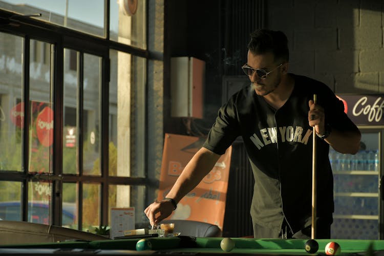 A Man In Black Shirt Smoking While Holding A Cue