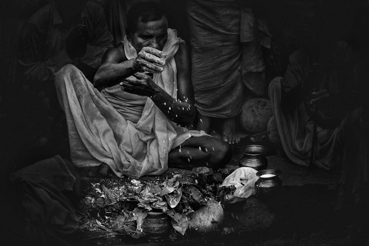 Black And White Photo Of Man Sprinkling Salt On Rags Lying On Ground