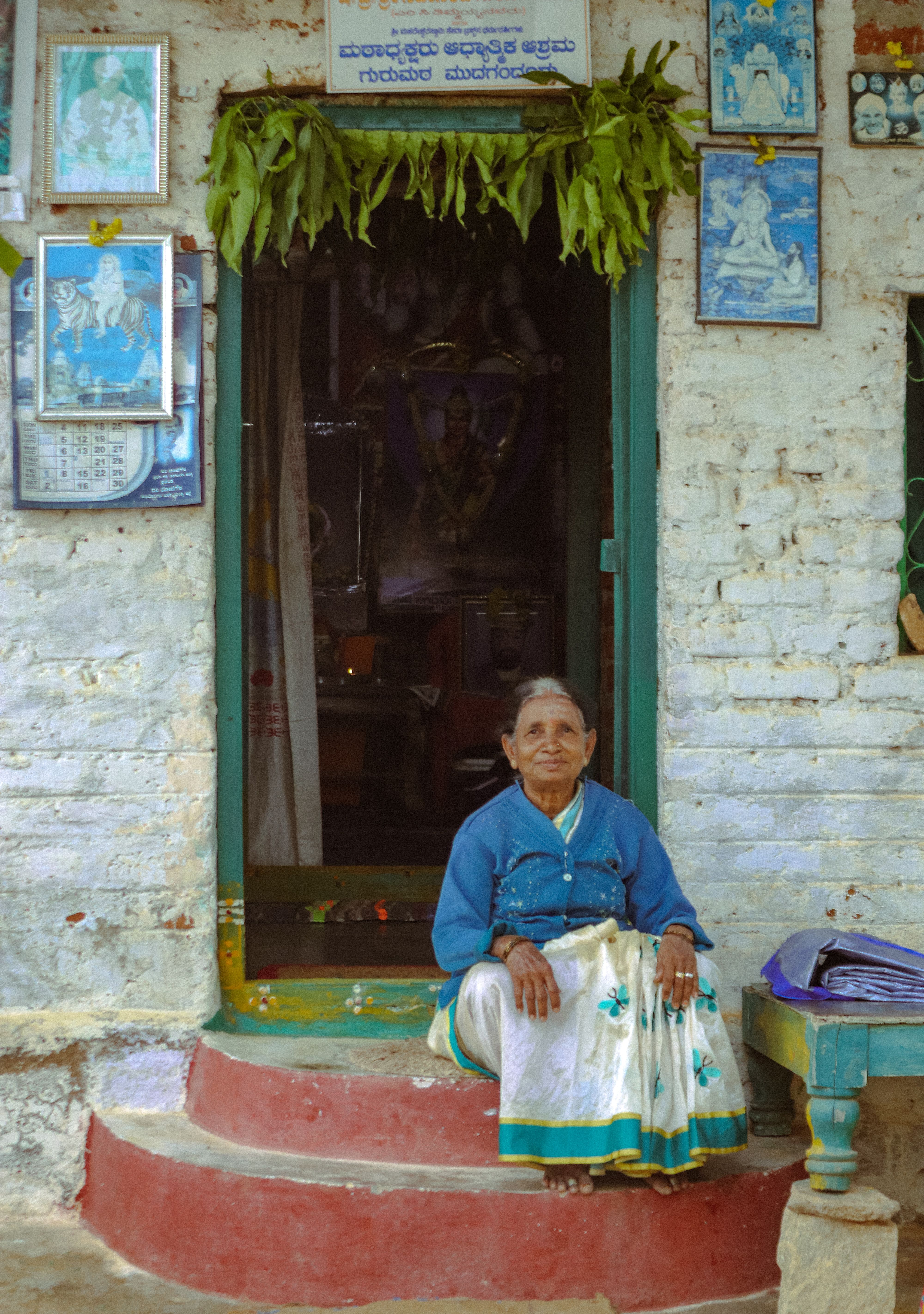 An elderly woman sits in front of a traditional village home in Mandya, India.