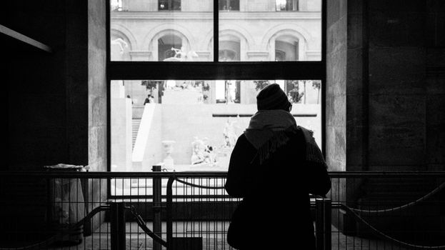 Black and white image of a person silhouetted against a museum window, reflecting architectural beauty.