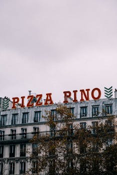 Neon PIZZA PINO sign atop a residential building in a cityscape.