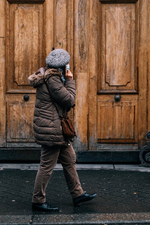 Woman in Winter Clothing Walking by a Wooden Door