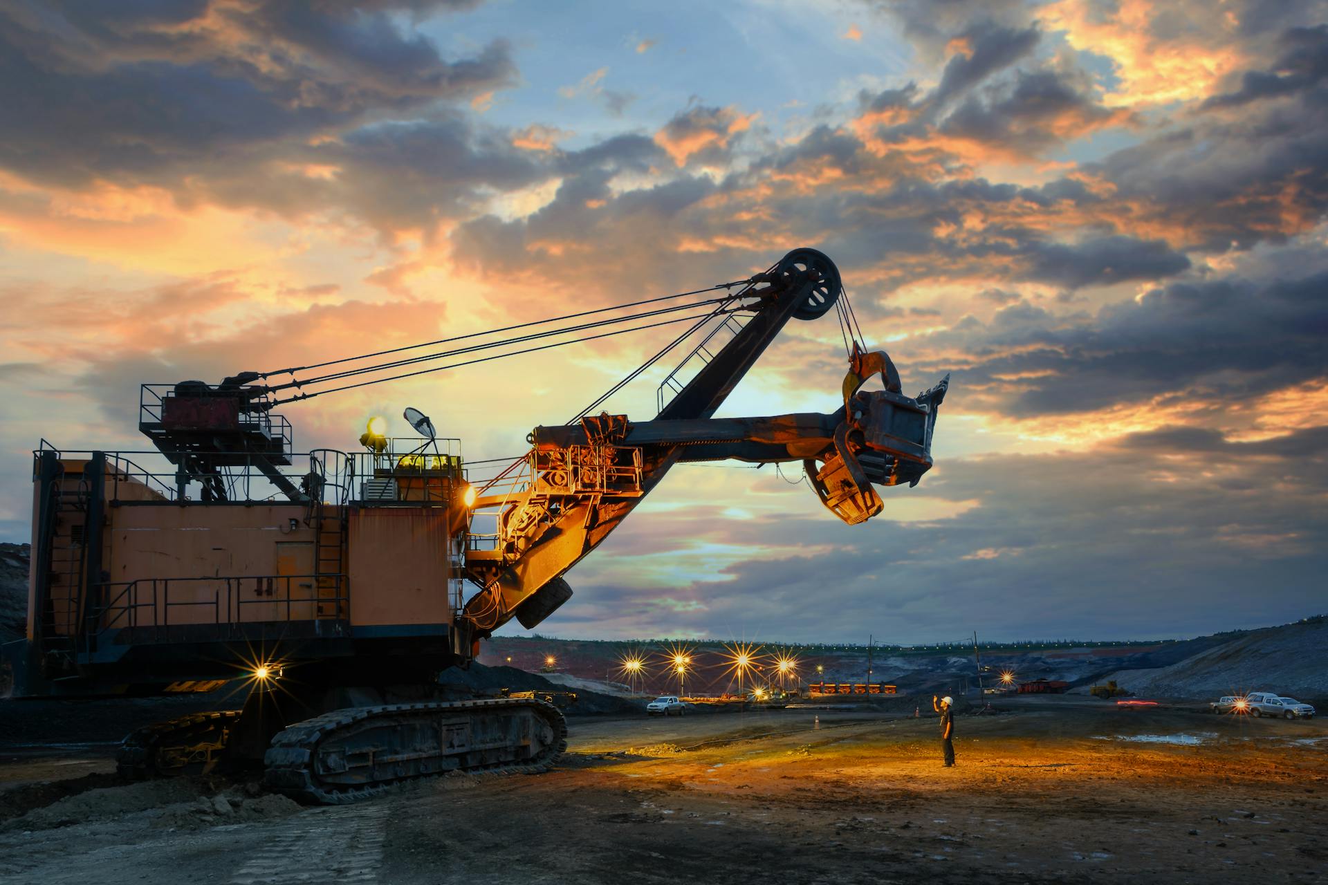 A powerful excavator dominates the landscape during a dramatic sunset, highlighting industrial activity.