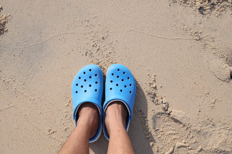 Person Wearing Blue Rubber Clogs Standing On Sand