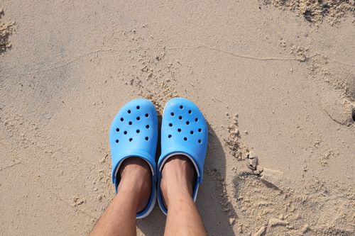 Free Blue rubber sandals on sandy beach, perfect for summer style and beach travel. Stock Photo