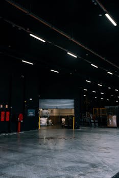 Dark and expansive industrial warehouse interior with overhead lights and open loading door.