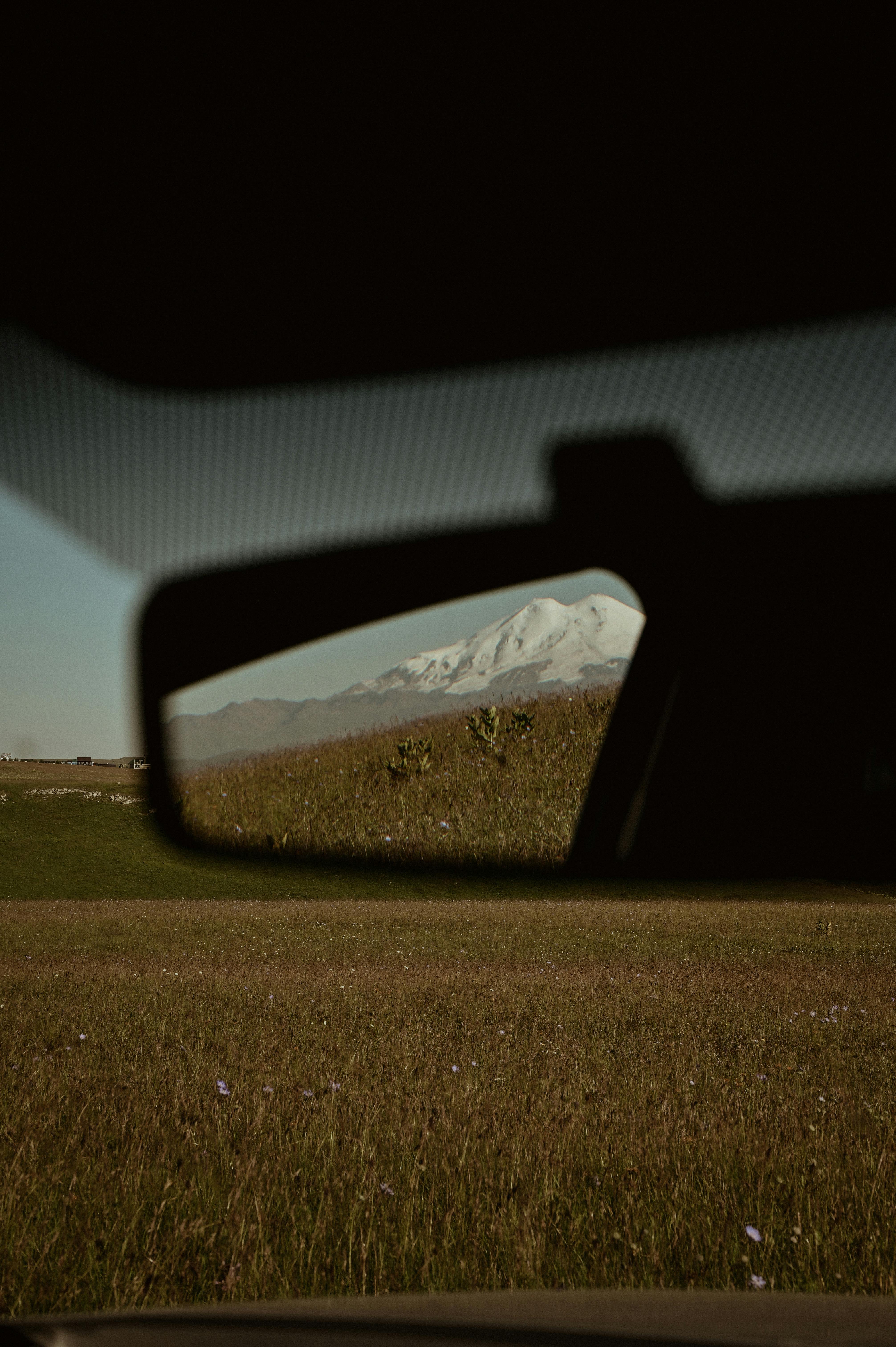 A scenic view of mountains through a car's rear view mirror, capturing nature's beauty.