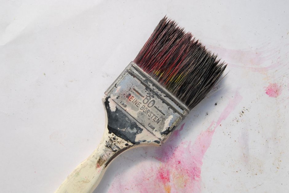 A detailed close-up of a weathered paintbrush with colorful bristles against a white background.