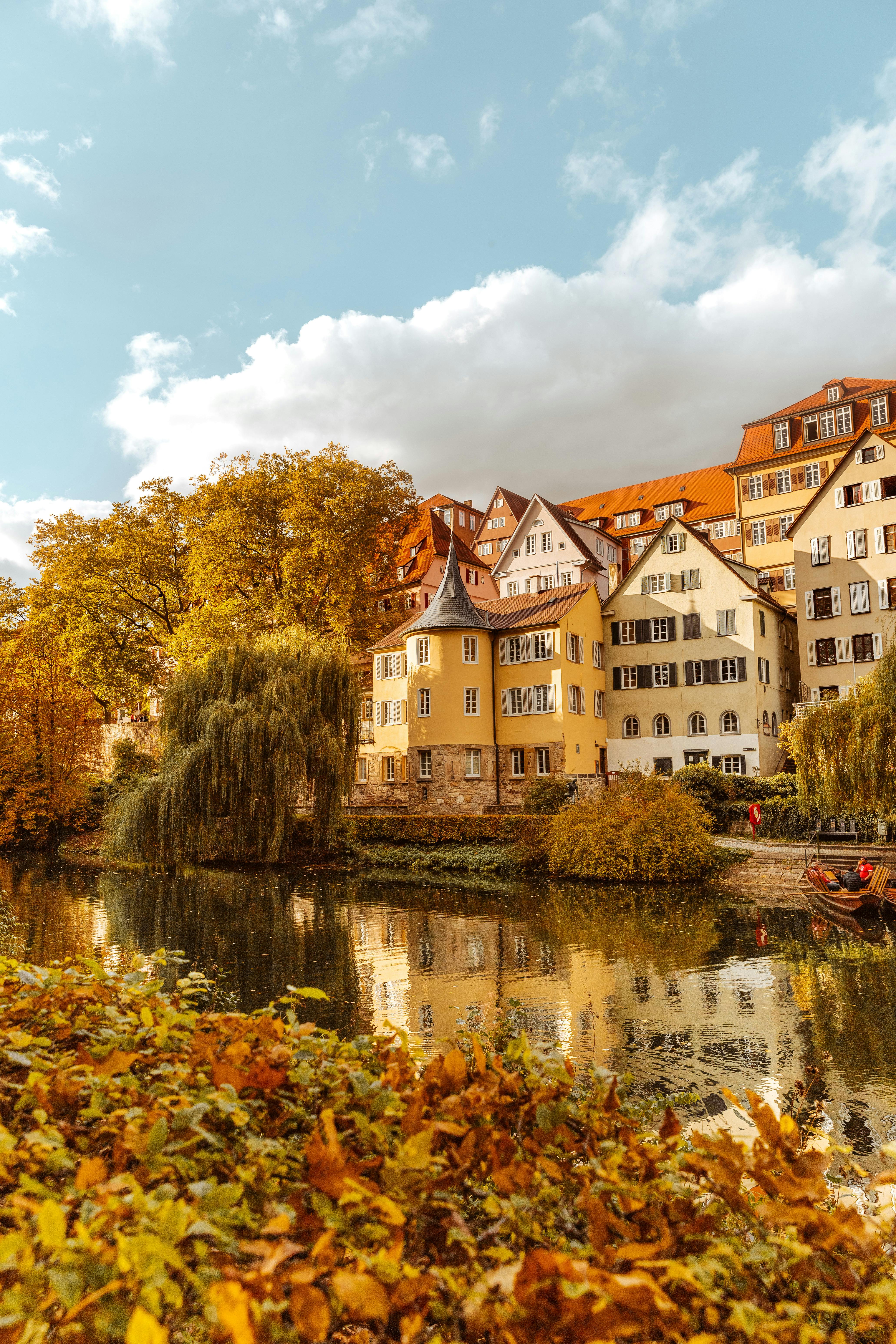 Picturesque riverside houses reflecting on water with vibrant autumn trees.