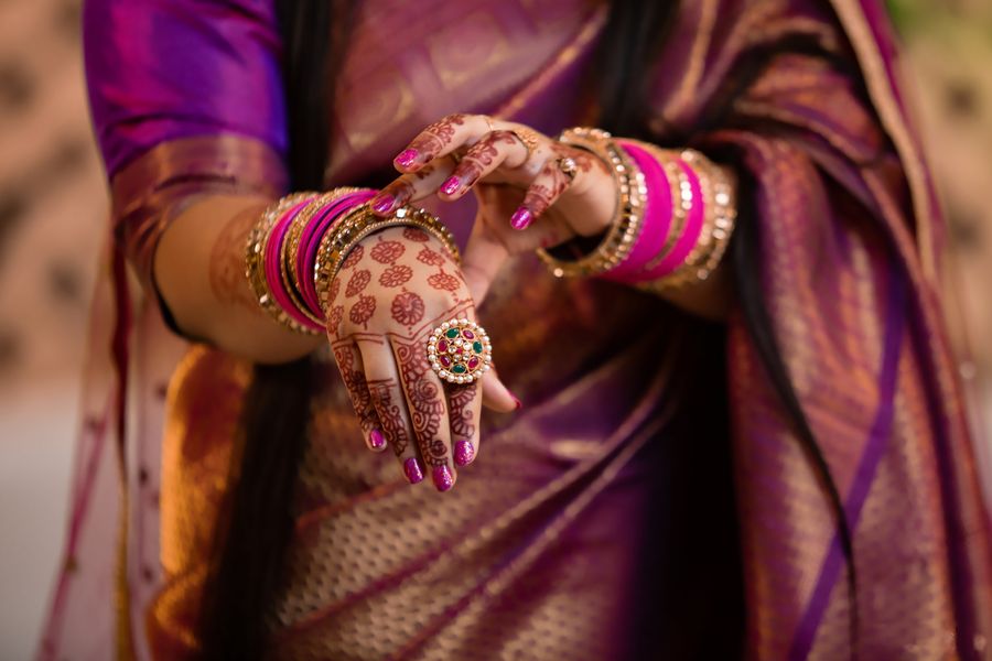 Henna-covered hand with pink bangles resting on purple silk