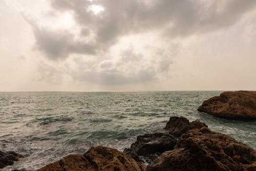 Cloudy seascape capturing the serene ocean and rocky shore under a dramatic sky.