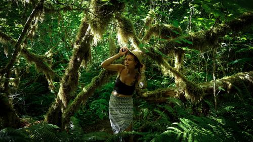 Free A woman in a black tank top and skirt explores a lush green rainforest under sunlight. Stock Photo