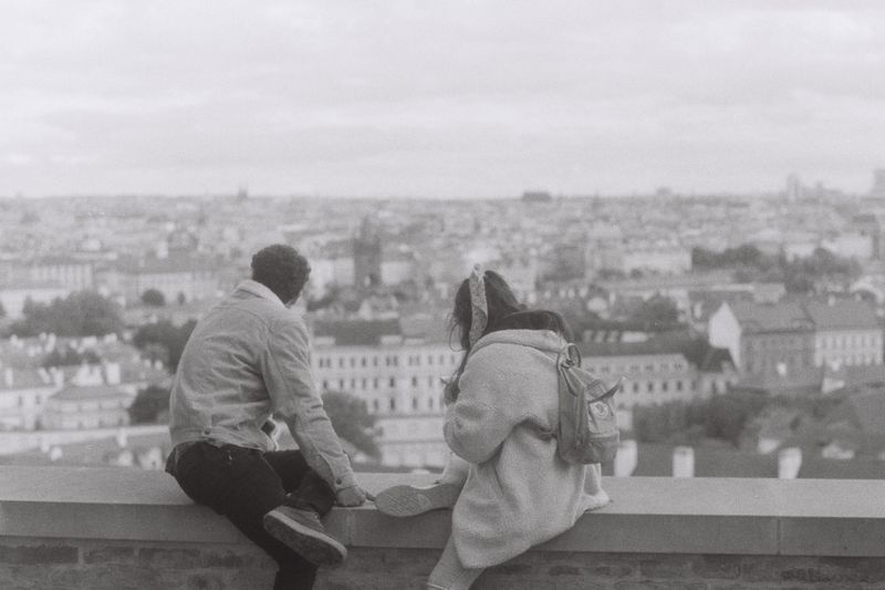 A couple sits on a ledge, overlooking a sprawling cityscape in a classic black and white photograph.