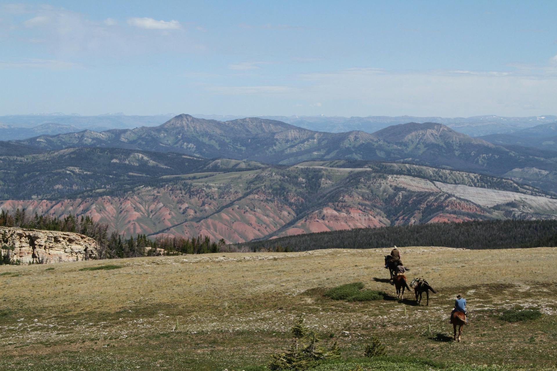 Experience the rugged beauty of Wyoming's mountains with riders on horseback under a clear sky.
