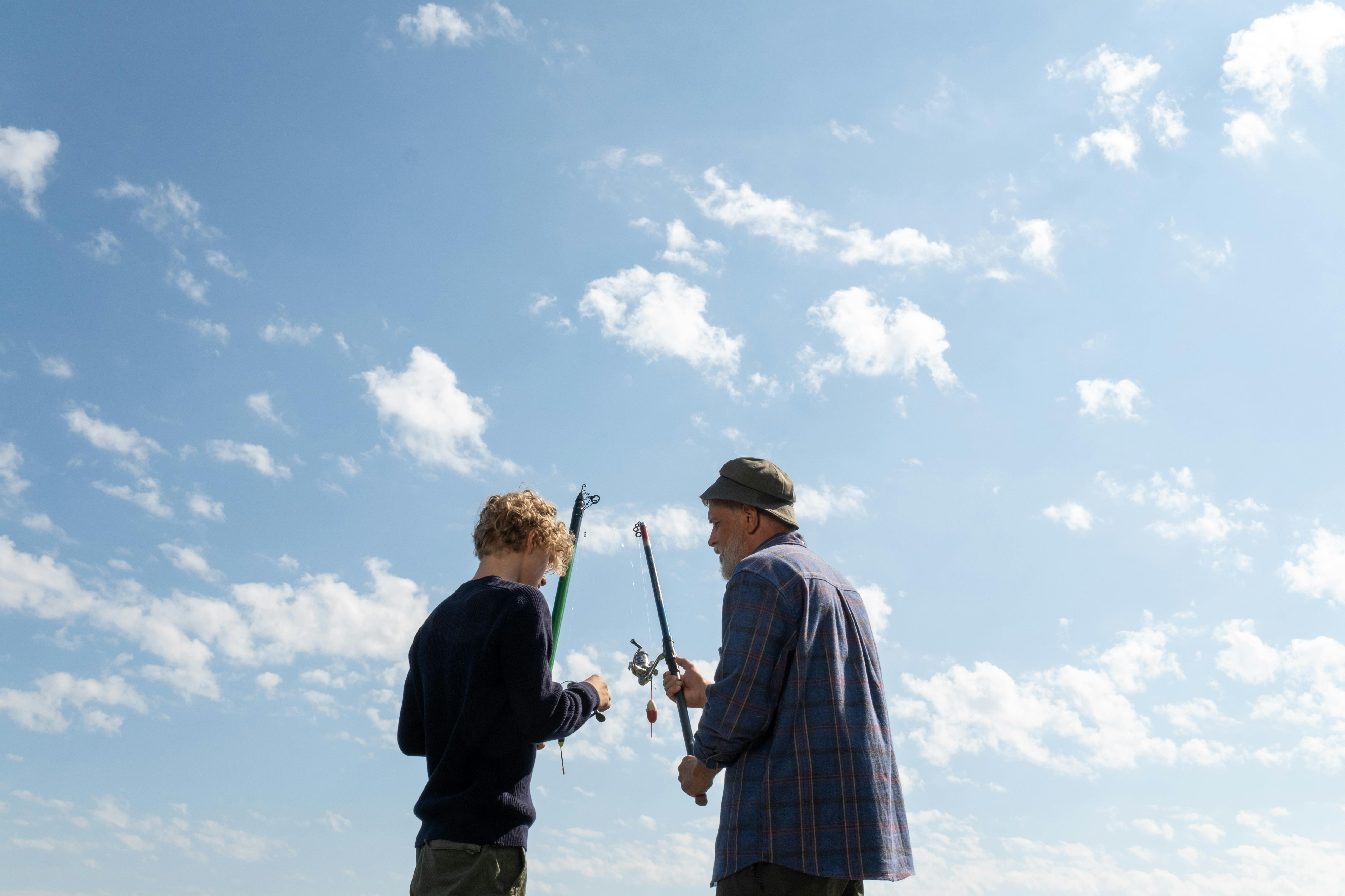 A senior adult and teenager fishing together under a bright blue sky.