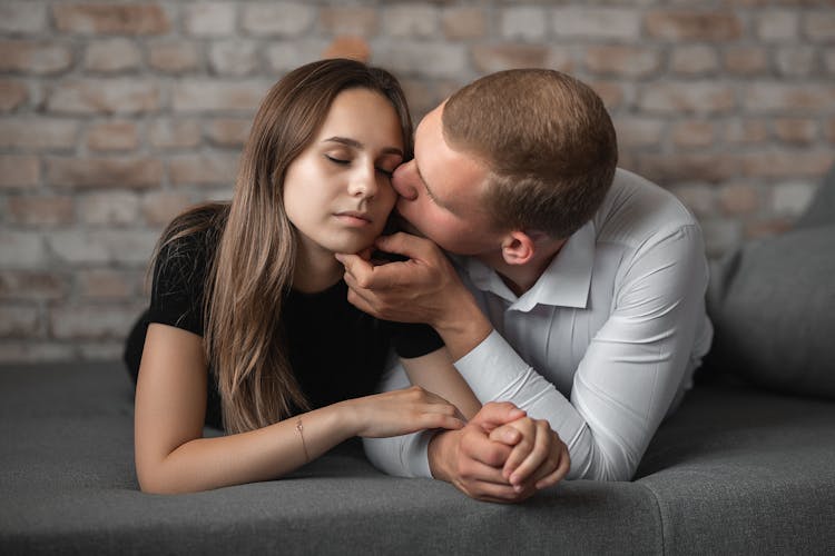 Young Man And Woman Holding Hands And Man Kissing Her In Cheek