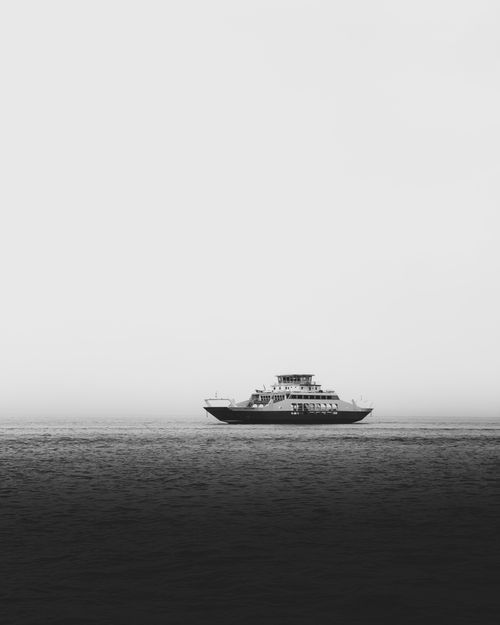 Free Elegant black and white image capturing a solitary ferry navigating the misty waters of Kuwait City. Stock Photo
