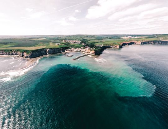 Aerial view of a harbour town beside a turquoise bay, photo by Lewis Ashton on Pexels