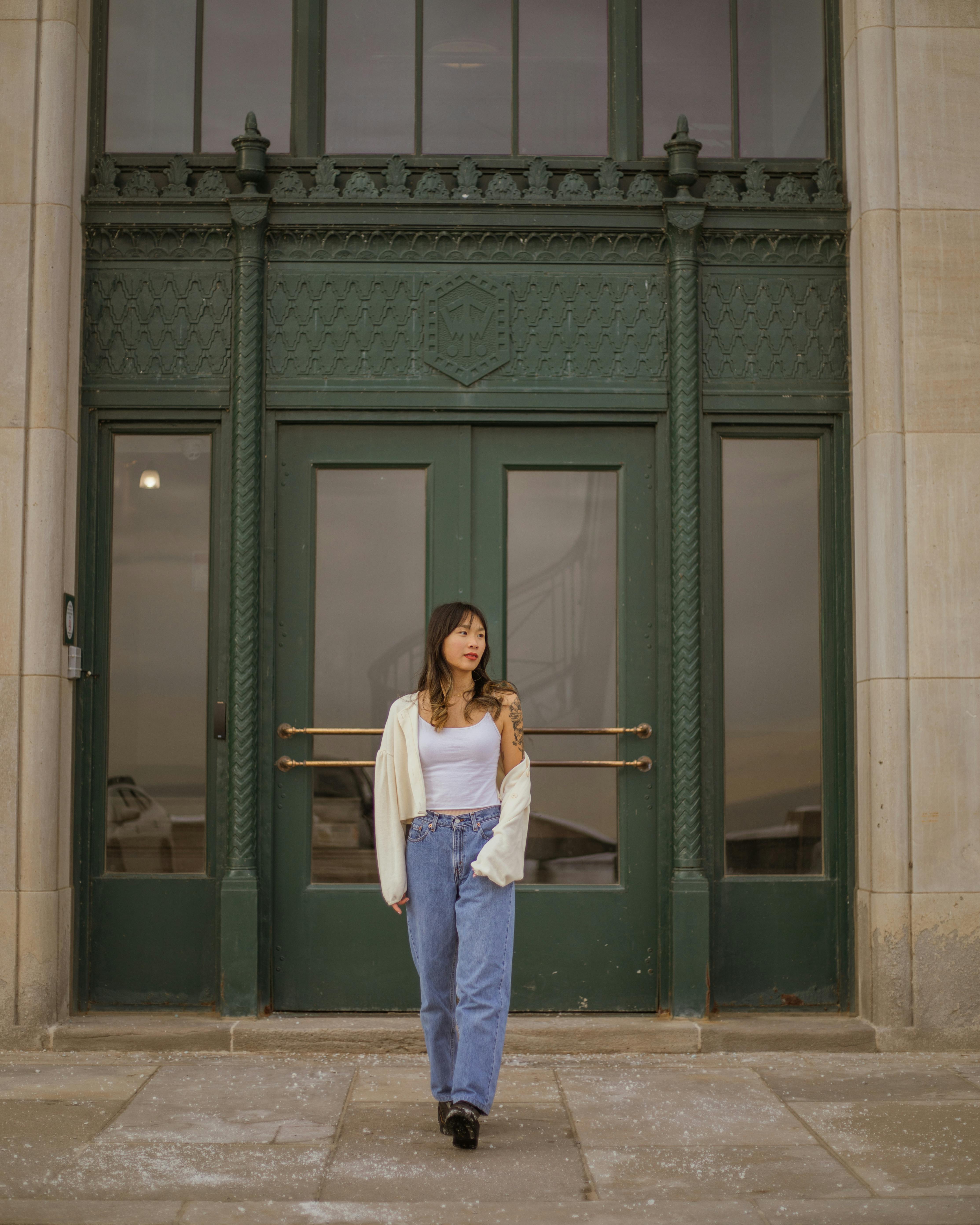 Young woman in casual attire standing confidently by an ornate green door, showcasing modern fashion.