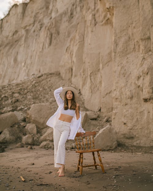 Free Woman in Hat Standing on Beach Leaning on Chair Stock Photo