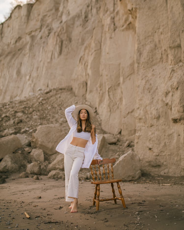 Woman In Hat Standing On Beach Leaning On Chair