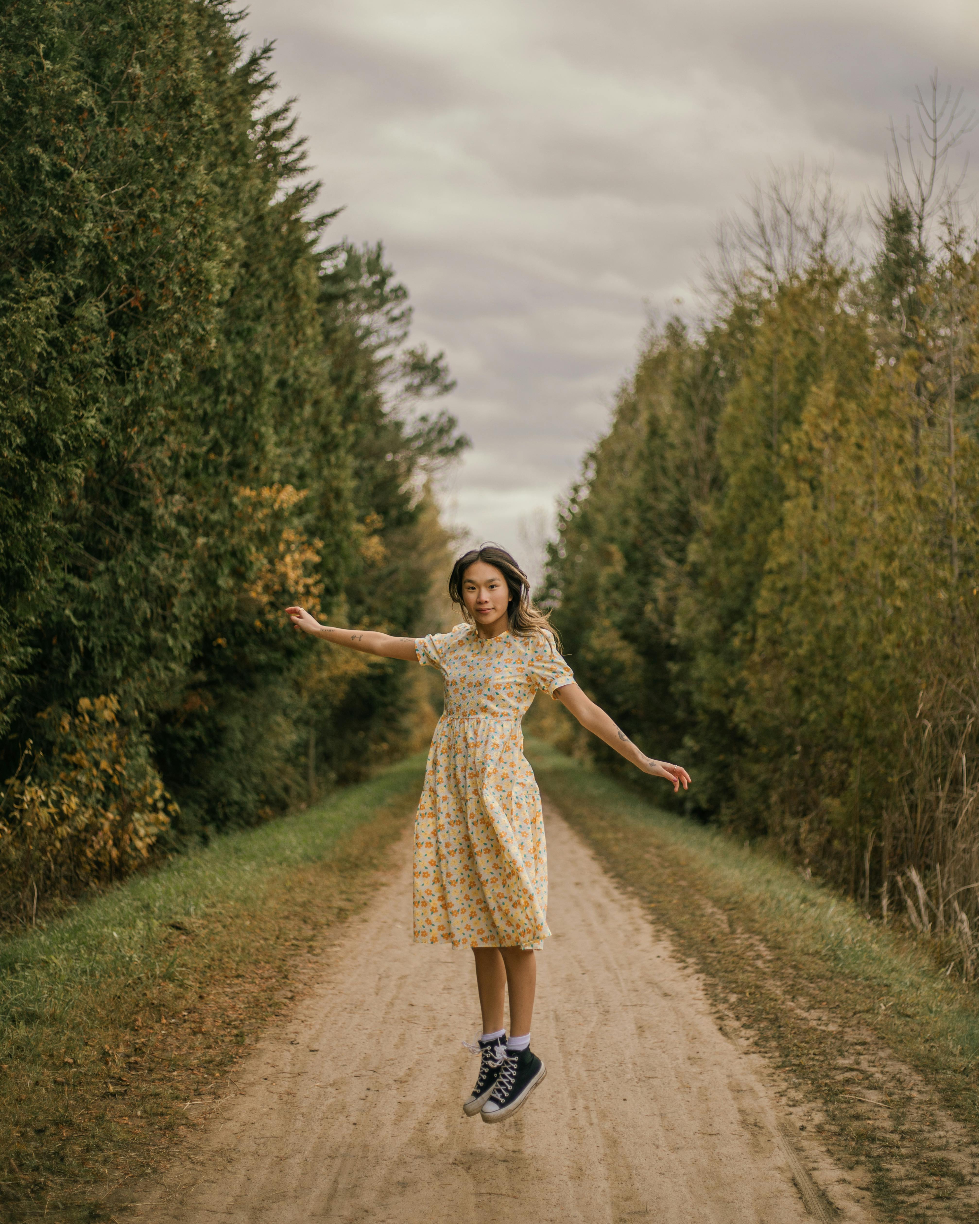 Young woman in floral dress jumps joyfully on a forest path during fall.