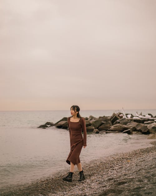 Woman in Brown Dress Walking on Seashore