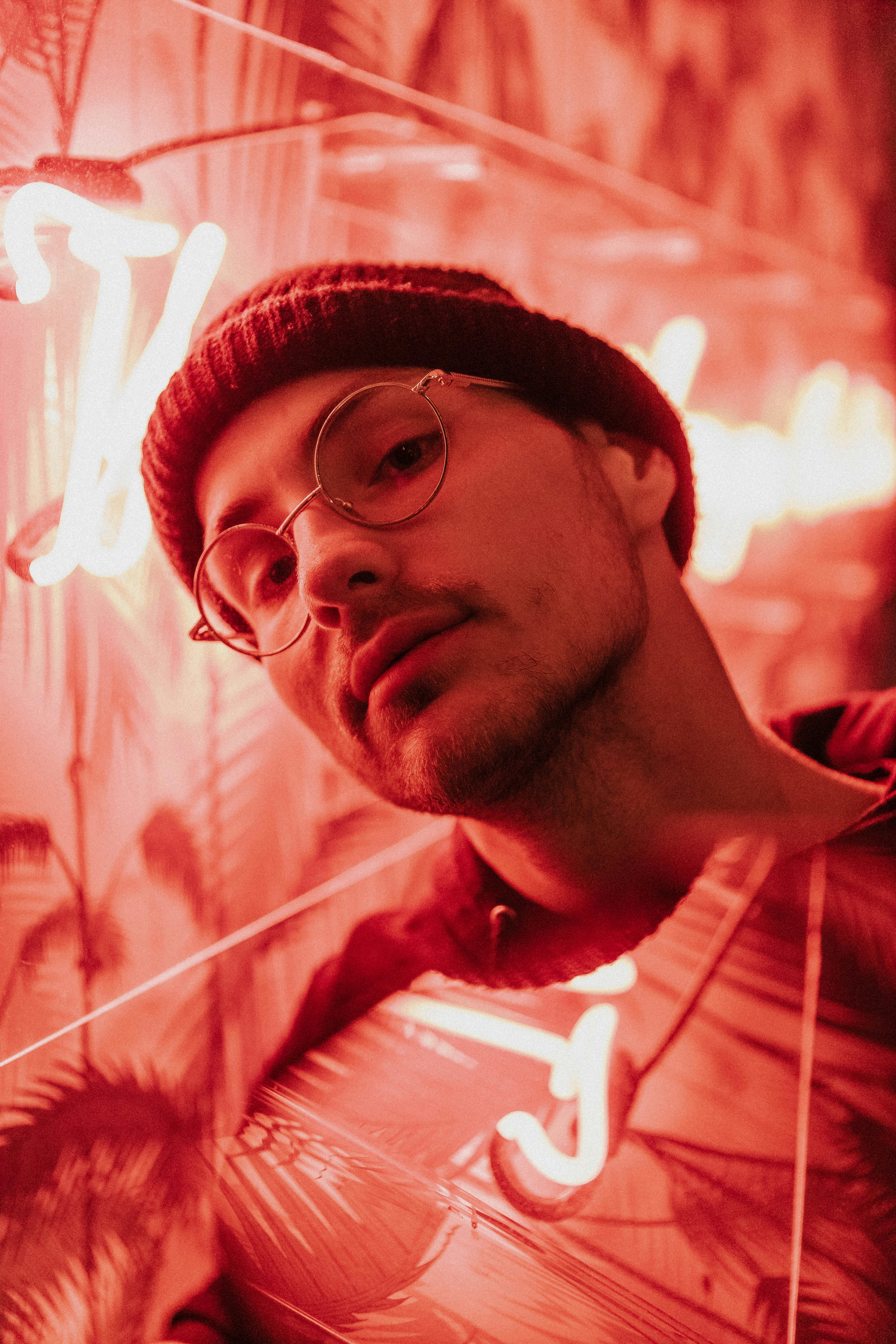 Stylish portrait of a man with glasses and beanie under vibrant neon lights.