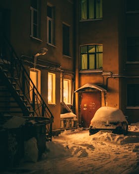 A cozy, snow-covered courtyard with lit windows on a winter night, exuding warmth and tranquility.