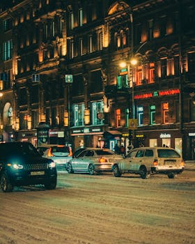 A snowy city street at night with cars and illuminated buildings, capturing a winter urban scene.