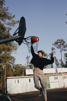 Man performs a slam dunk on an outdoor basketball court surrounded by trees.