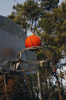 Close-up of a basketball hoop and ball on an outdoor court during daytime.