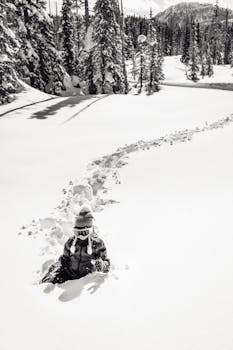Child in winter gear playing in deep snow with trail in snowy BC forest.