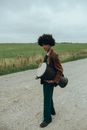 Woman in Brown Leather Jacket and Black Pants Carrying White Hat Walking on Gray Sand during