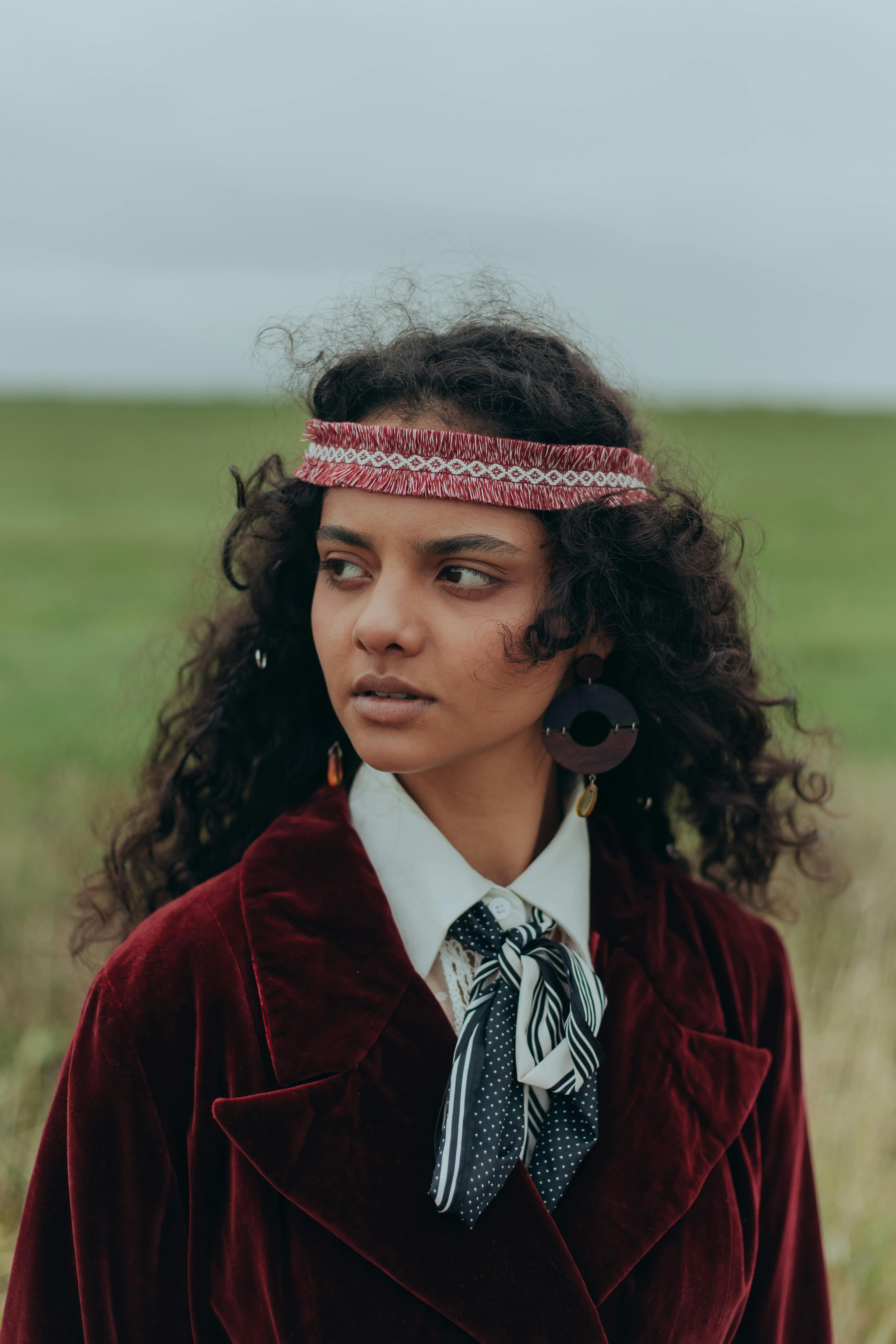 Portrait of a woman in vintage hippie attire with a headband in a natural setting.